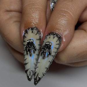 ongles pointus de pouces avec des squelettes de main argentées sur fond blanc